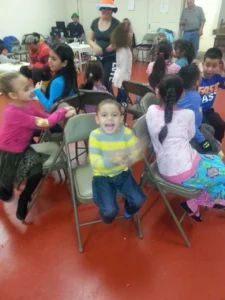 A room filled with children on chairs, accompanied by adults who are interacting with them