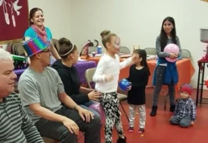 A diverse group of individuals seated on chairs and some individuals are standing holding colorful balloon