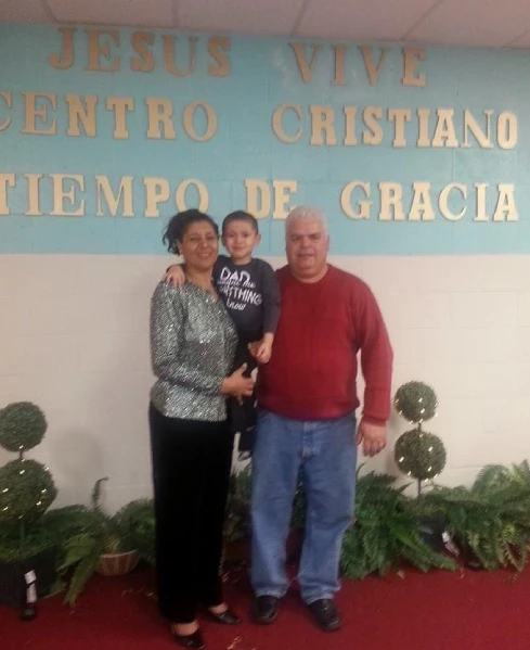 A family of three, consisting of a man, woman, and child, poses in front of a church, symbolizing community and togetherness